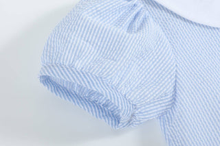 Close-up of a blue and white checkered shirt with rolled-up sleeves on a light gray background