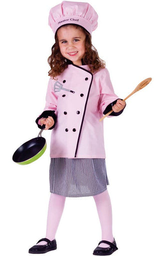 A young girl modeling a pink children's chef costume consisting of a double-breasted jacket, striped skirt, and matching chef hat, while holding a toy pan and wooden spoon against a white background.