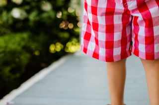 Person wearing red and white checkered shorts on a blurred outdoor background