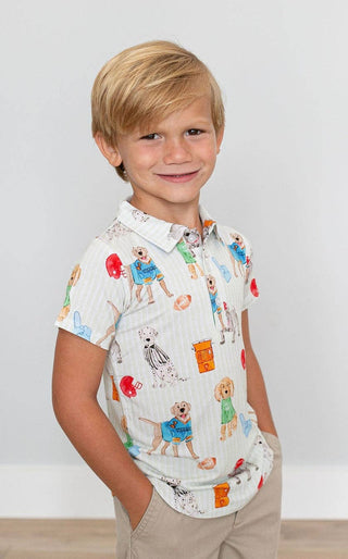 A child wearing a white polo shirt with a watercolor design featuring various animals, predominantly dogs, engaging in football-themed activities.