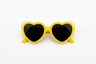 Heart-shaped sunglasses with bright yellow frames and dark brown lenses, photographed against a clean white background.
