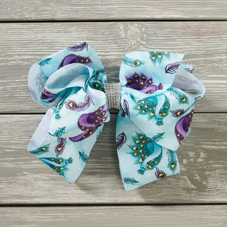 A blue hair bow with a pattern of peacocks and ornamental feathers.