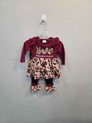 A toddler girl's long-sleeve dress hanging on a clear plastic hanger against a plain gray wall. The dress features a dark burgundy top with a 'Peace Love Football' graphic and a tiered skirt with a brown, beige, and black leopard print patterned with footballs and rabbits.